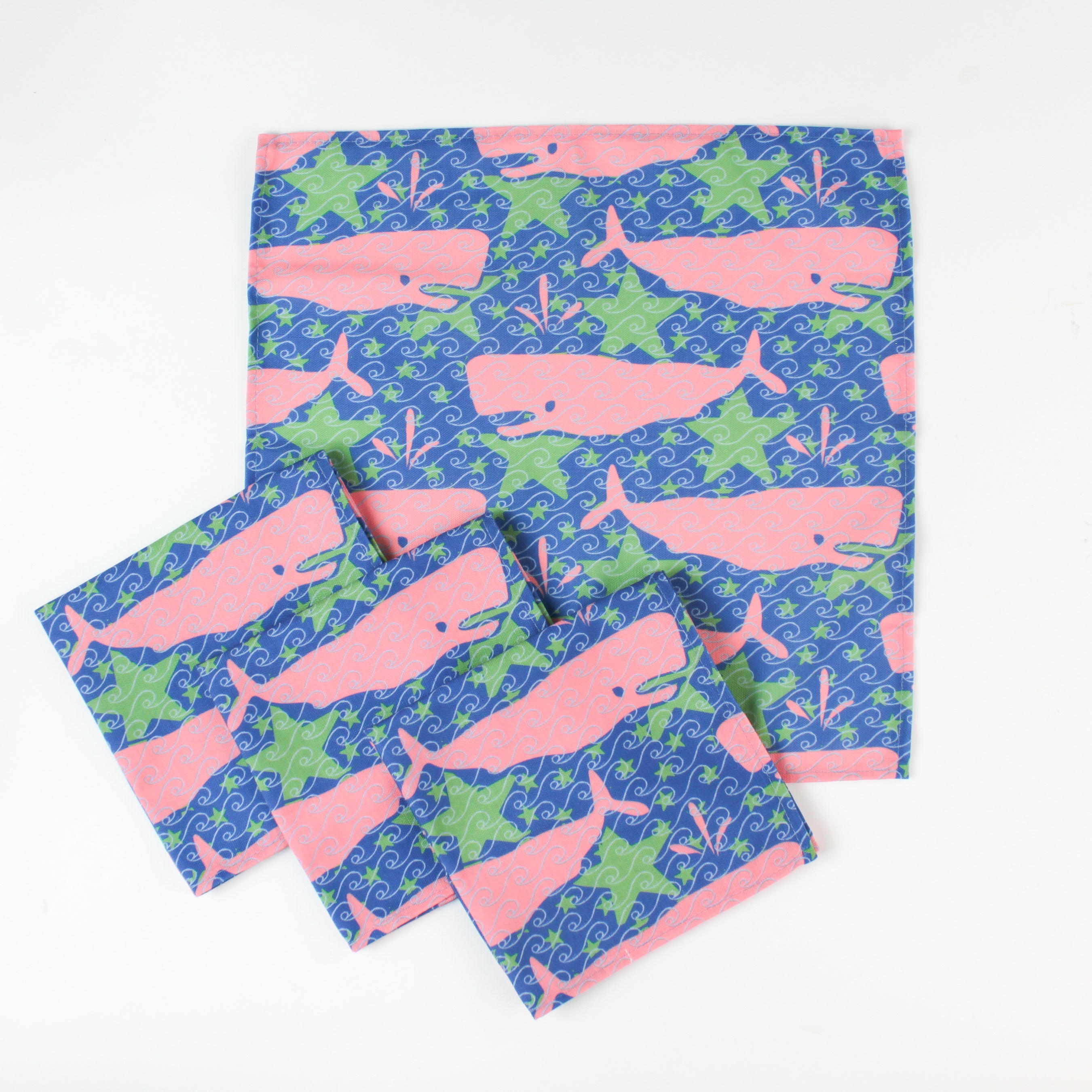 Set of cloth napkins with pink whale and green seaweed pattern on a blue background.
