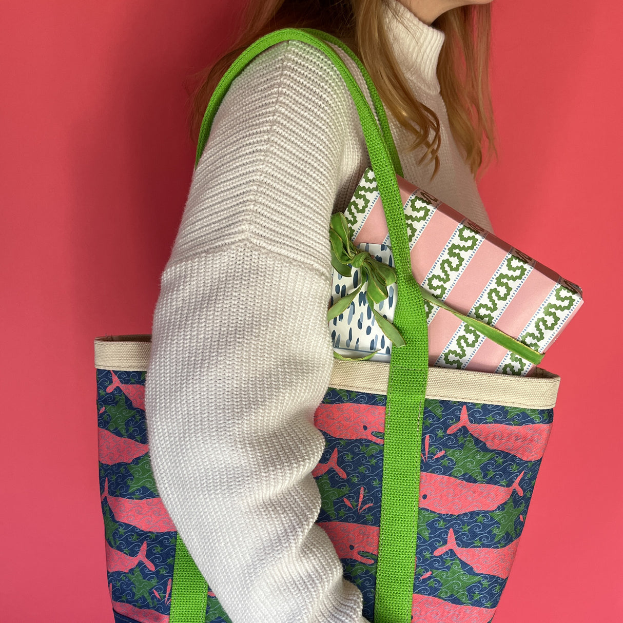 Whale of a Time canvas tote bag with lime straps and blue fabric with a repeating pink whale  and green star motif on models shoulder.