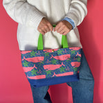 Whale of a Time canvas small tote bag with lime straps and blue fabric with a repeating pink whale  and green star motif being held by model.
