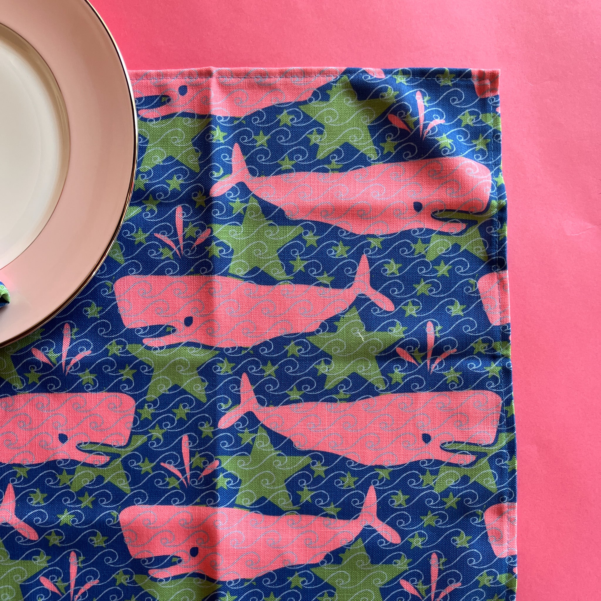 Close-up view of pink whale and green star patterned Whale of a Time cloth dinner napkin.