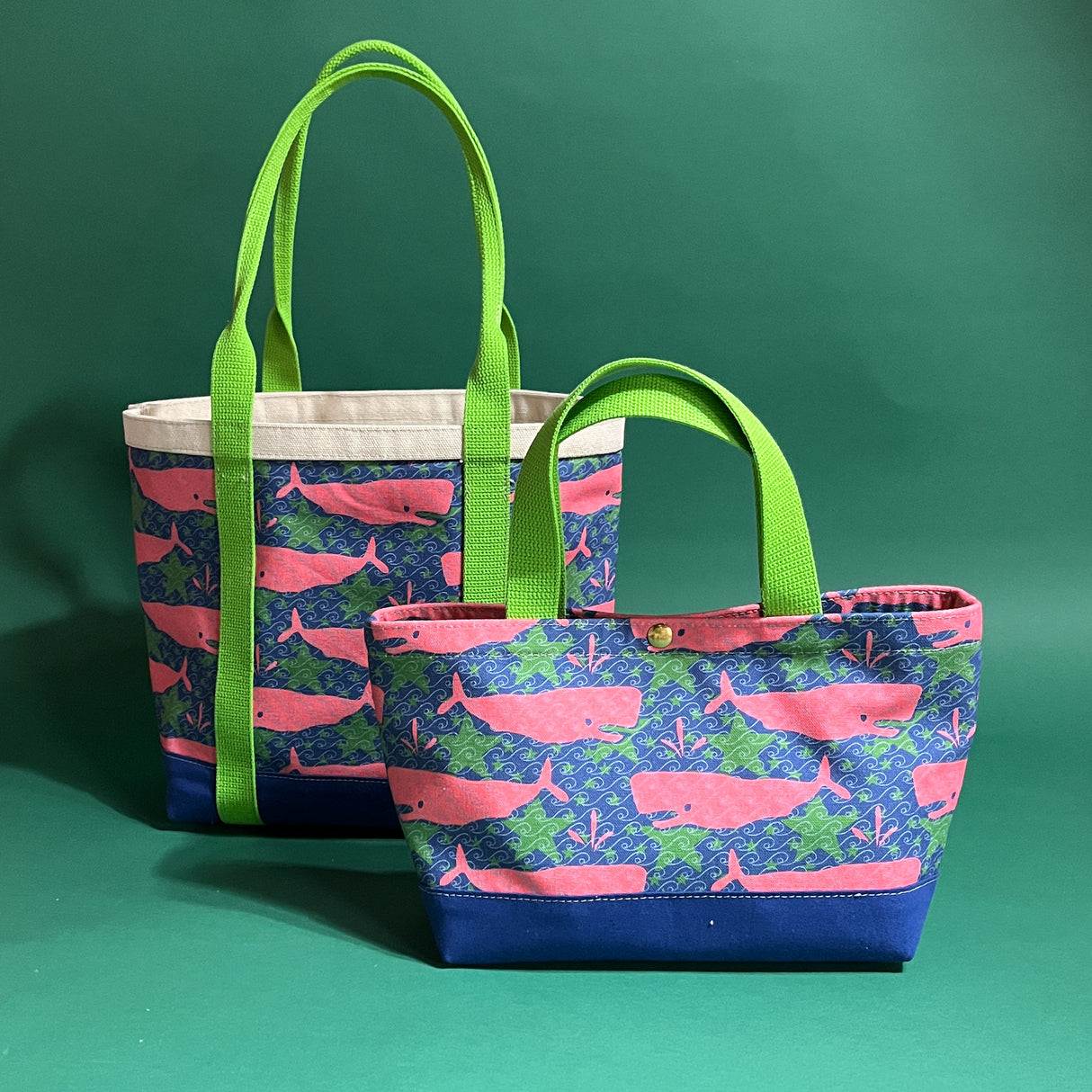 Two canvas tote bags with lime straps and fabric with a repeating pink whale motif. 