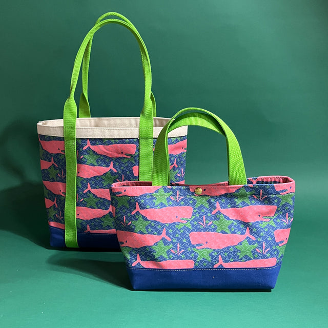 Two canvas tote bags with lime straps and fabric with a repeating pink whale motif. 