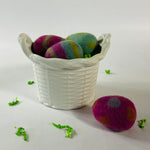 White ceramic basket with scalloped rim styled with colorful felt eggs and green filler