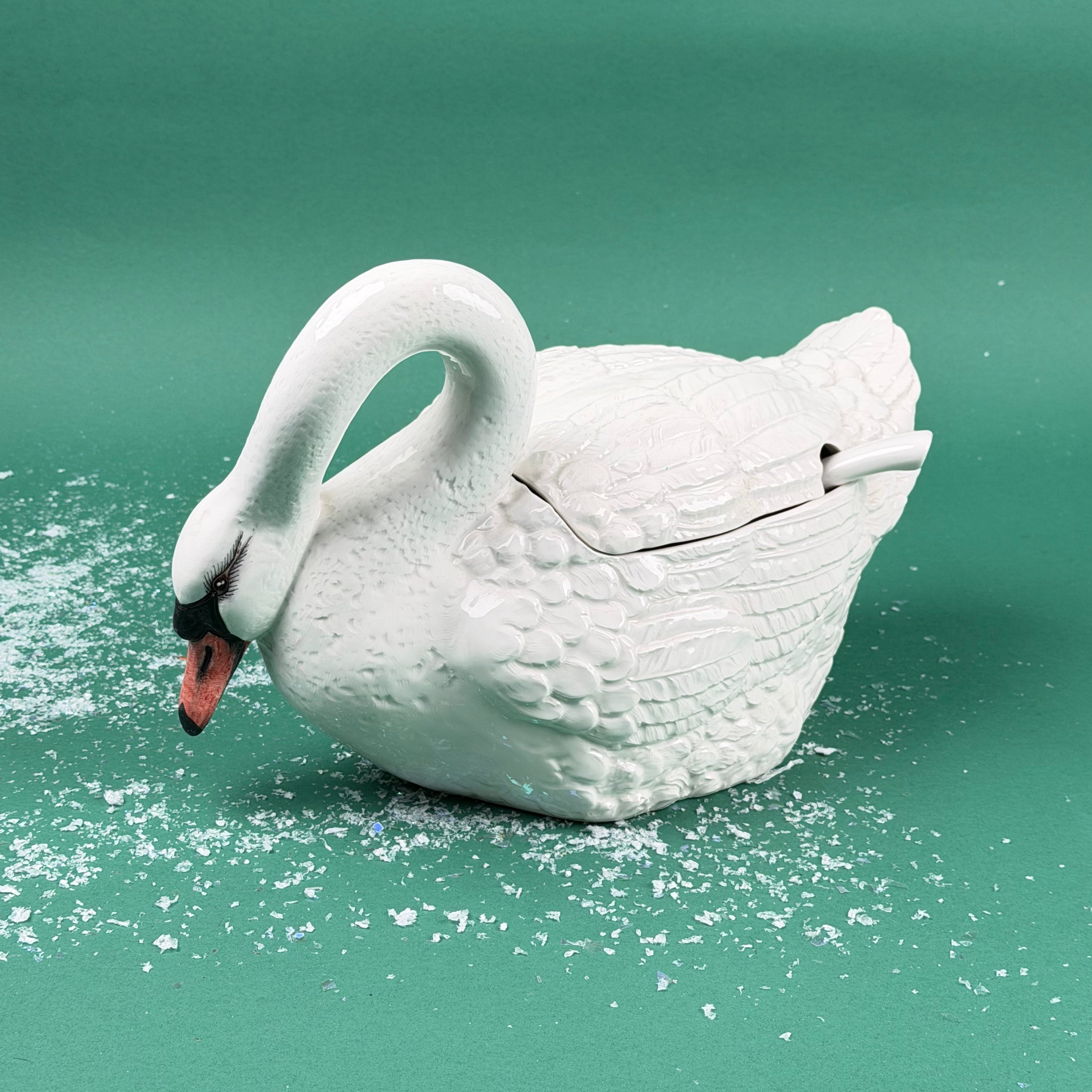 White ceramic swan-shaped soup tureen with lid and ladle on a green background with faux snow