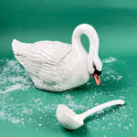White ceramic swan-shaped soup tureen with matching ladle on a green background with faux snow
