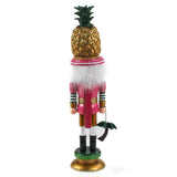  back view of a 19.5" tall Yellow and Pink Christmas Nutcracker Table Decoration with a gold pineapple hat and  holding a palm tree against a white background. 