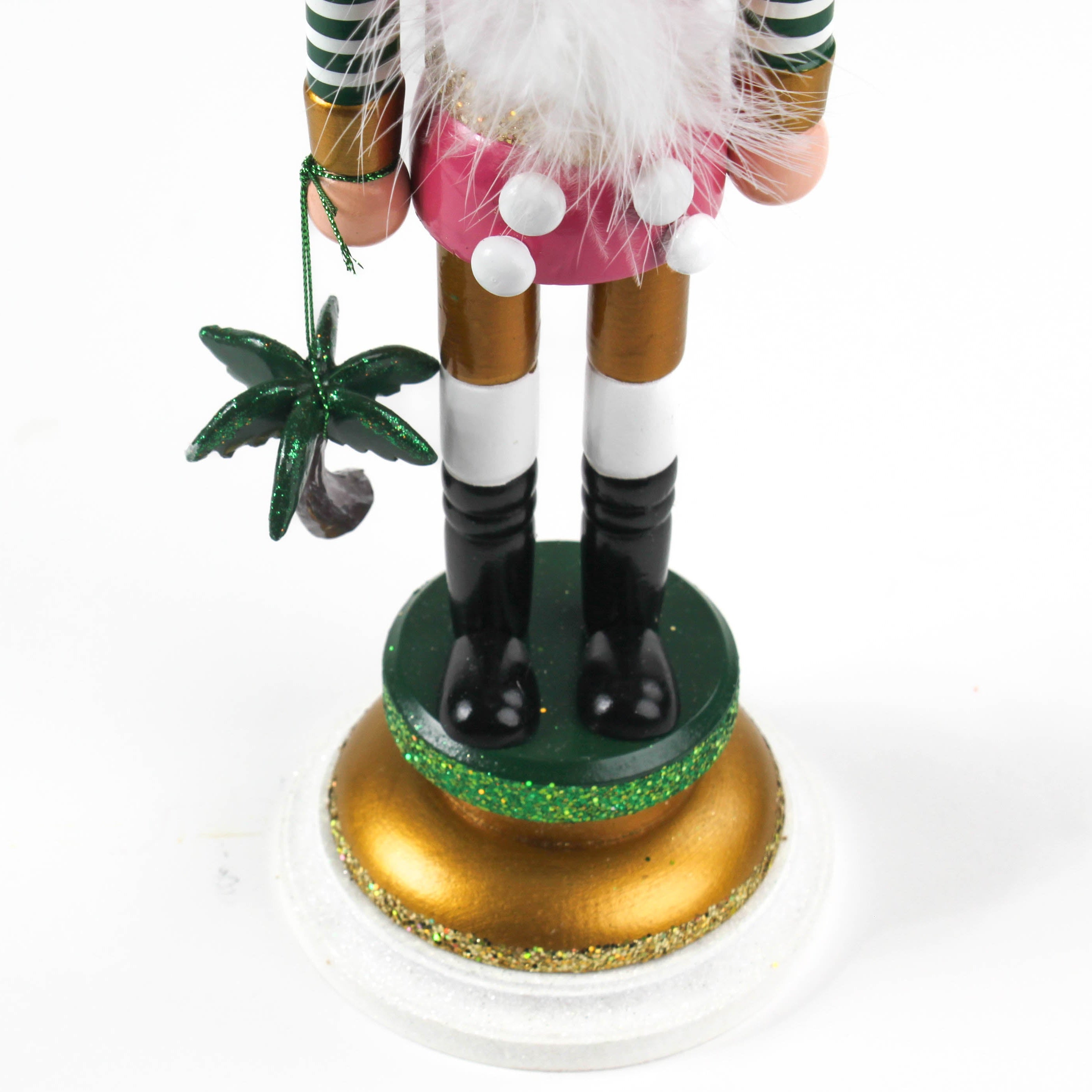 a close up shot showing the feet of a 19.5" tall Yellow and Pink Christmas Nutcracker Table Decoration with a gold pineapple hat and  holding a palm tree against a white background. 