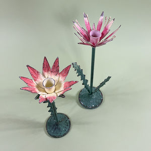 Two metal flower candle holders in the shape of a lotus flower with pink petals and green stems