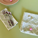 light green cloth dinner napkins in bahama court trellis print madcap cottage fabric next to a pink plate with cutlery resting on top.