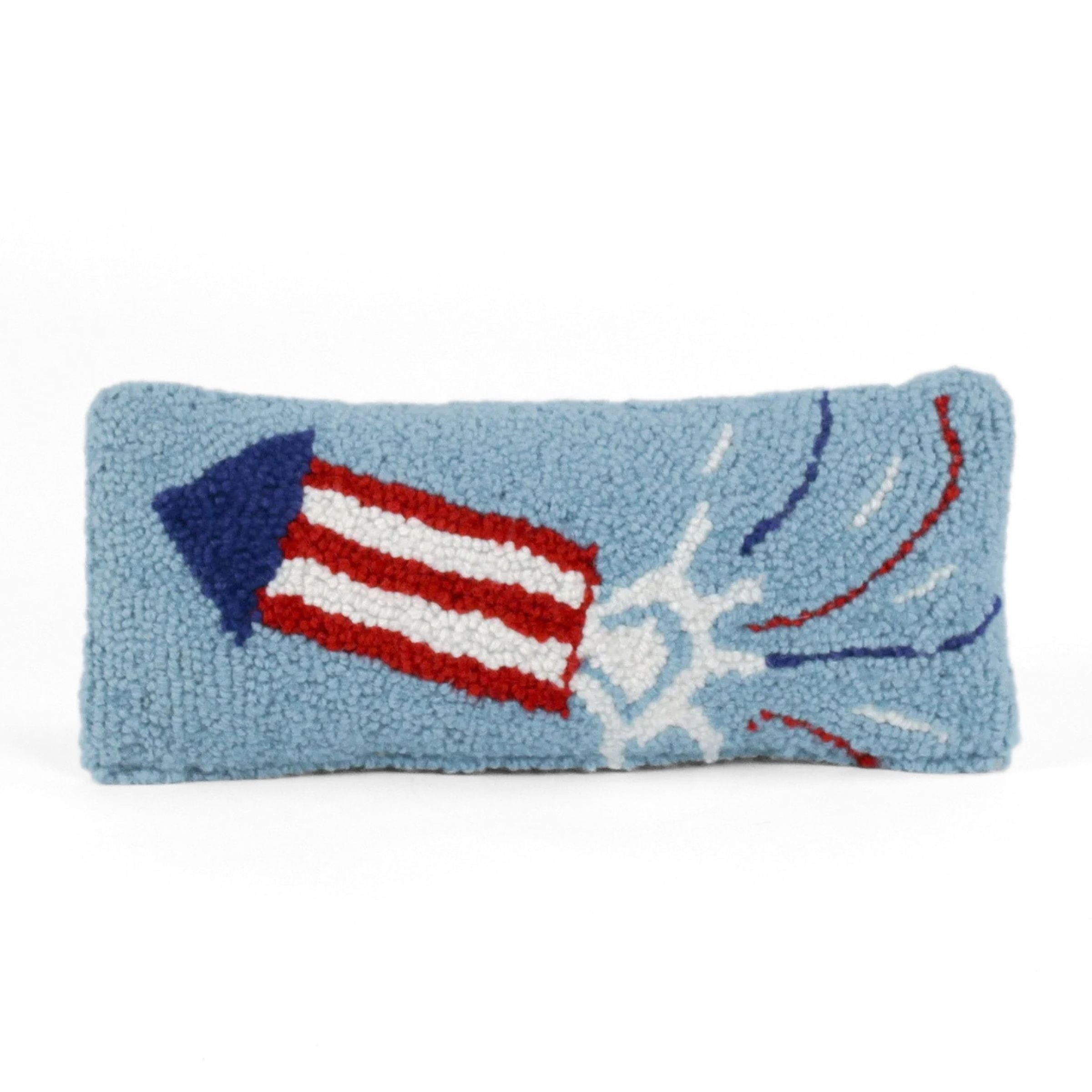 Rectangular blue decorative pillow with a hooked texture featuring a red, white, and blue fireworks rocket design, shown on a white background.