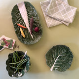 three cabbage leaf bowls filled with assorted vegetables resting on a light green background
