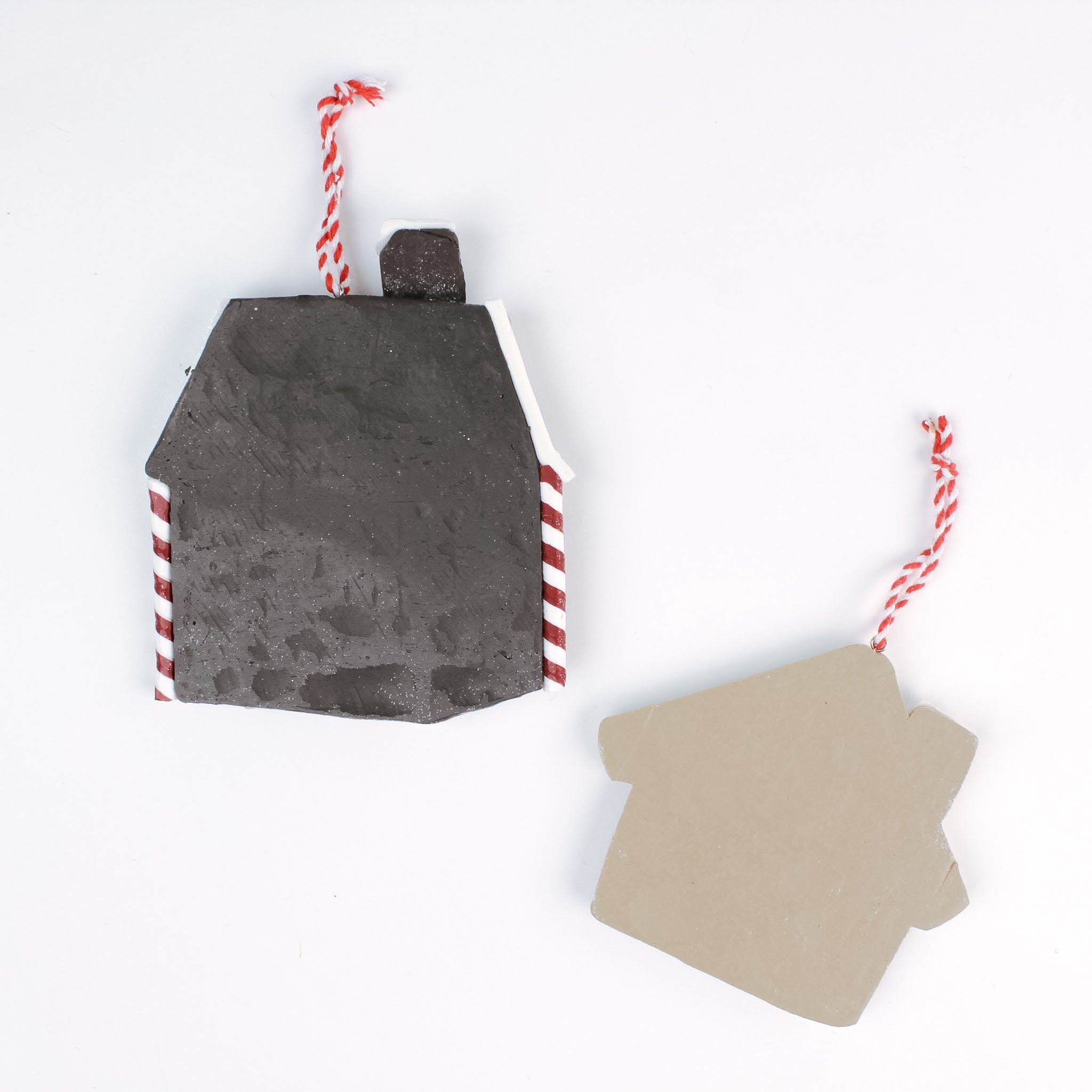 back of the Two gingerbread house Christmas ornaments, one pink and one brown with candy cane details, shown with red and white hanging strings in white background