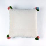 back of a Square hooked wool christmas pillow featuring a green Christmas ornament with red, pink, and blue patterns on a white background with a light blue scalloped border and colorful pom-poms on each corner.
