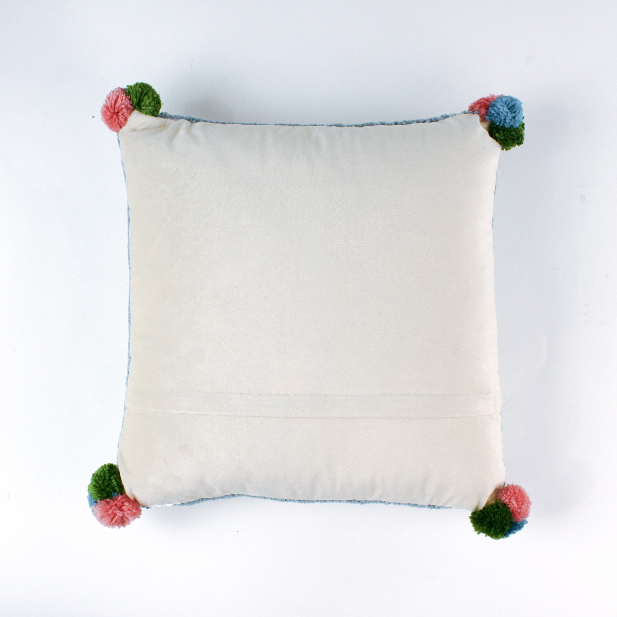 back of a Square hooked wool christmas pillow featuring a green Christmas ornament with red, pink, and blue patterns on a white background with a light blue scalloped border and colorful pom-poms on each corner.