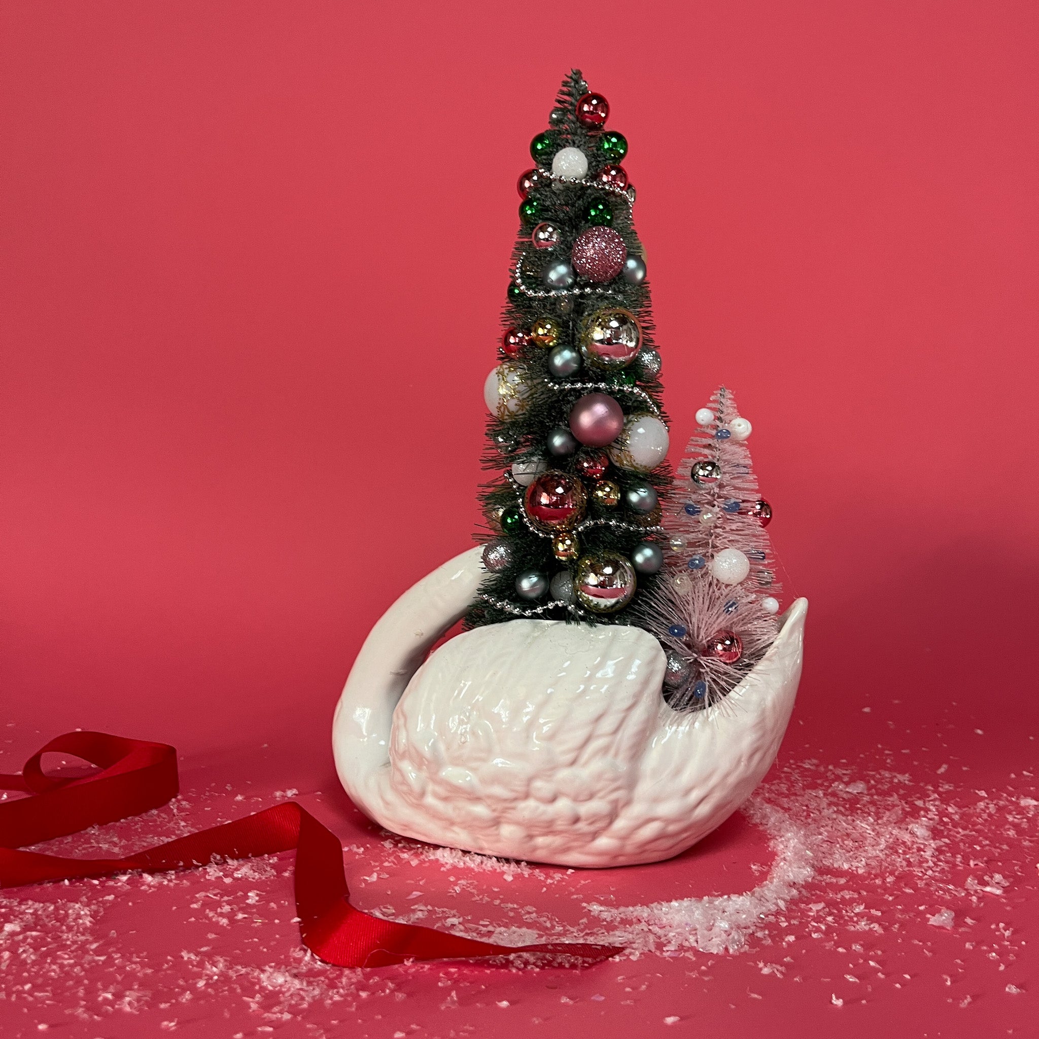 the back of a white Vintage Arched-Neck Ceramic Swan w/ a Pink/Purple/Gold Christmas Tree inside it against a red background. 