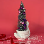 back of a white Vintage Arched-Neck Ceramic Swan w/ a Pink/Purple/Silver Christmas Tree inside it against a red background. 