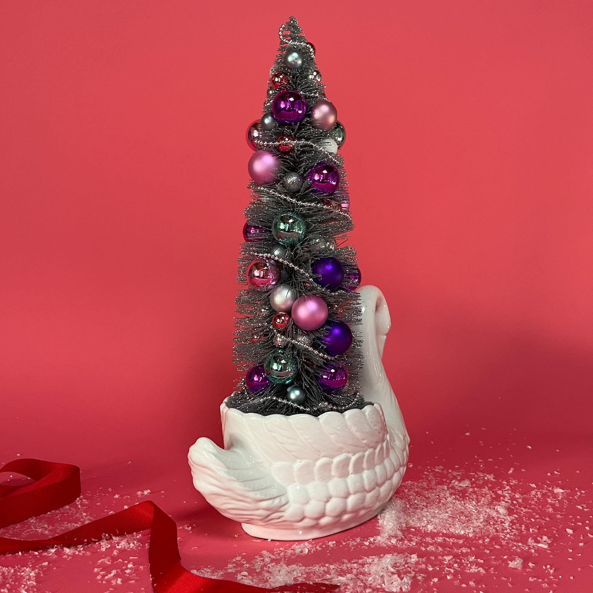 back of a white Vintage Arched-Neck Ceramic Swan w/ a Pink/Purple/Silver Christmas Tree inside it against a red background. 