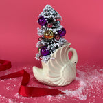 back of a white Vintage Small Arched-Neck Ceramic Swan w/ Gold/Purple Frosted Christmas Tree inside it against a red background. 