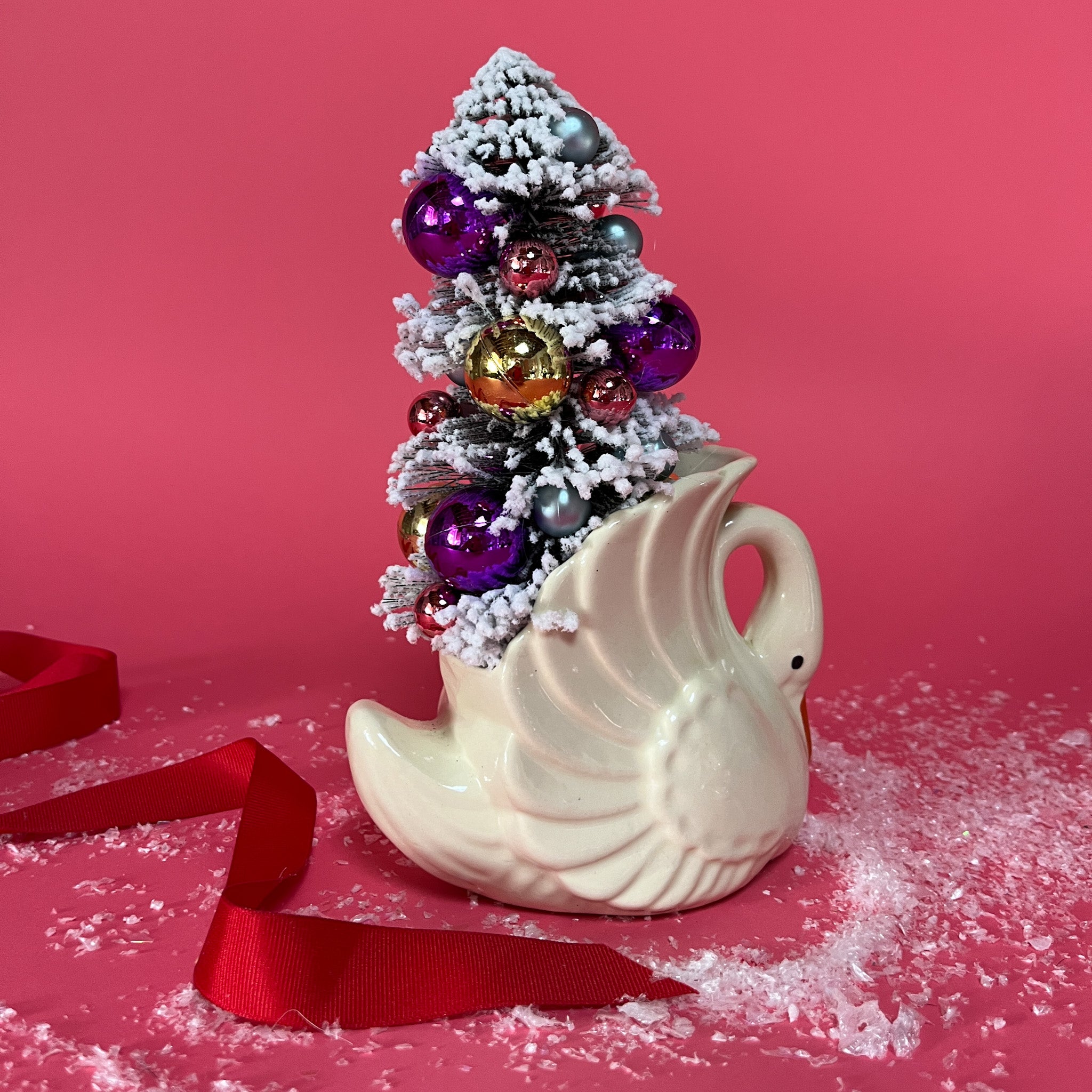 back of a white Vintage Small Arched-Neck Ceramic Swan w/ Gold/Purple Frosted Christmas Tree inside it against a red background. 