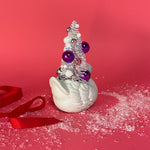 back of a Vintage Small White Ceramic Swan w/ Pink/Purple Glitter Christmas Tree Centerpiece against a red background