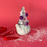 back of a Vintage Small White Ceramic Swan w/ Pink/Purple Glitter Christmas Tree Centerpiece against a red background