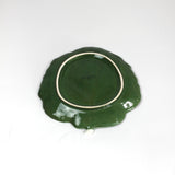 the underside of a ceramic green cabbage leaf plate on a white background.
