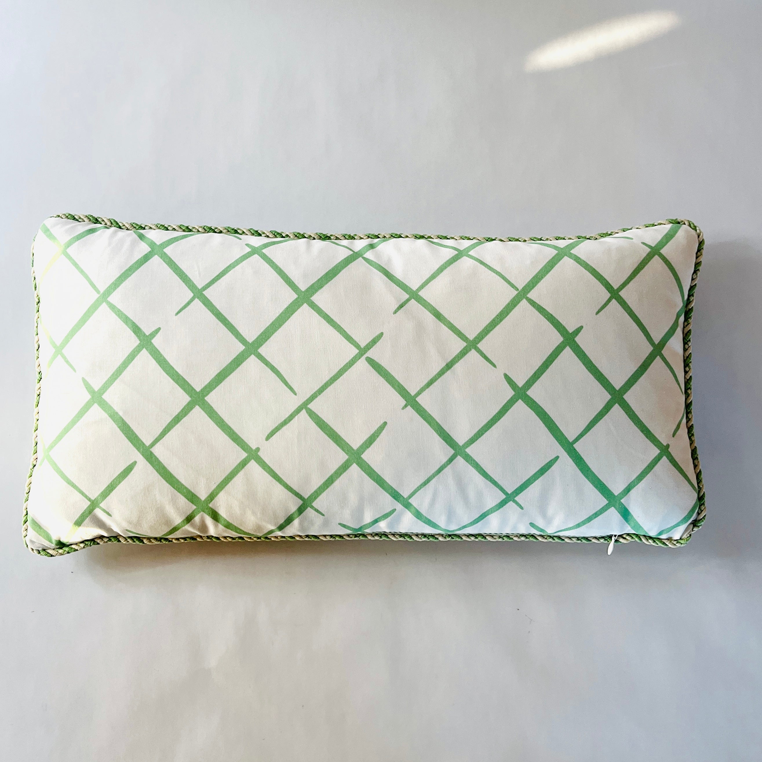 a green and white throw pillow with a criss cross motif and green piping.