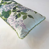a corner detail of a light blue throw pillow made from hydrangea print fabric and green cord piping.