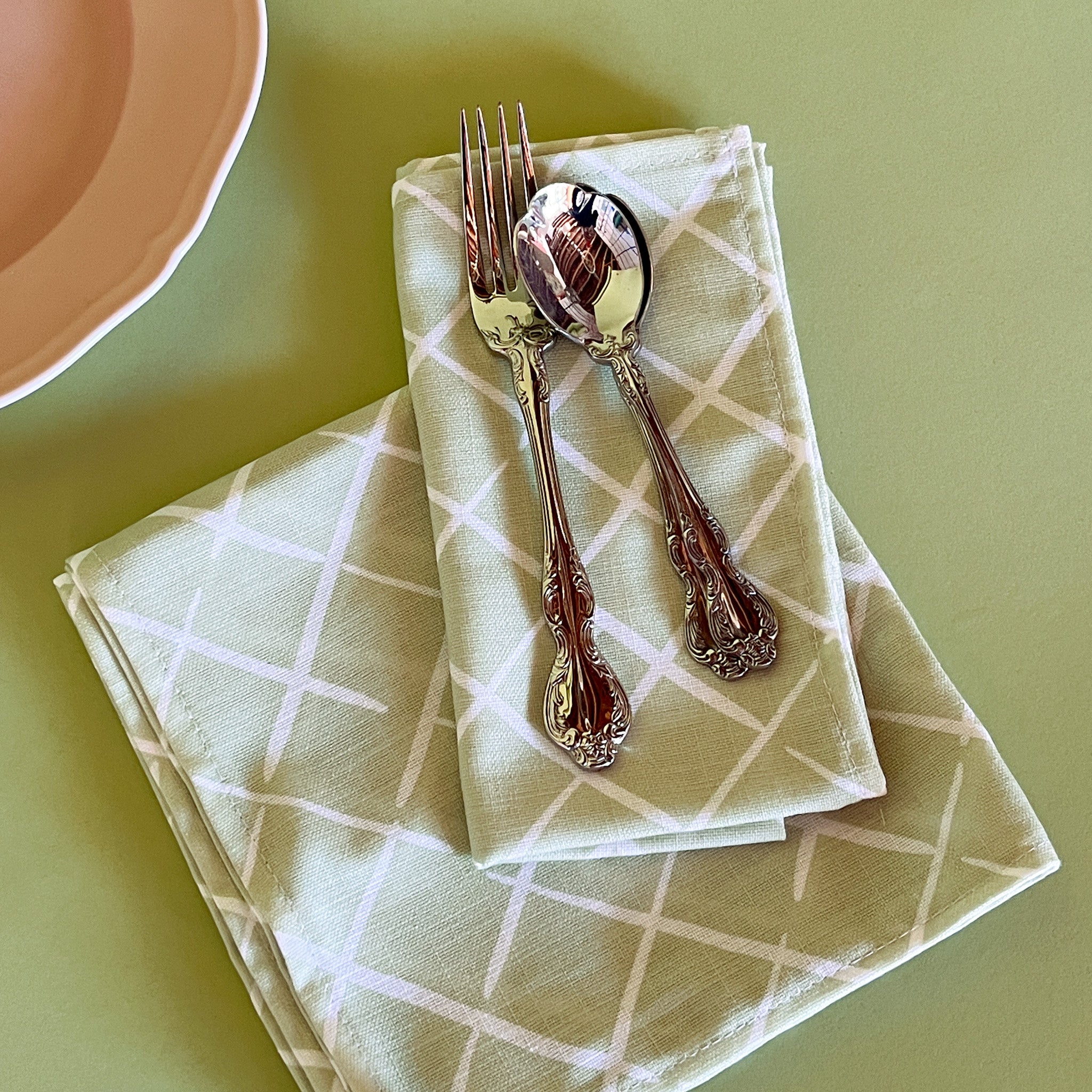 light green dinner napkins in bahama court trellis print madcap cottage fabric next to a pink plate with cutlery resting on top.