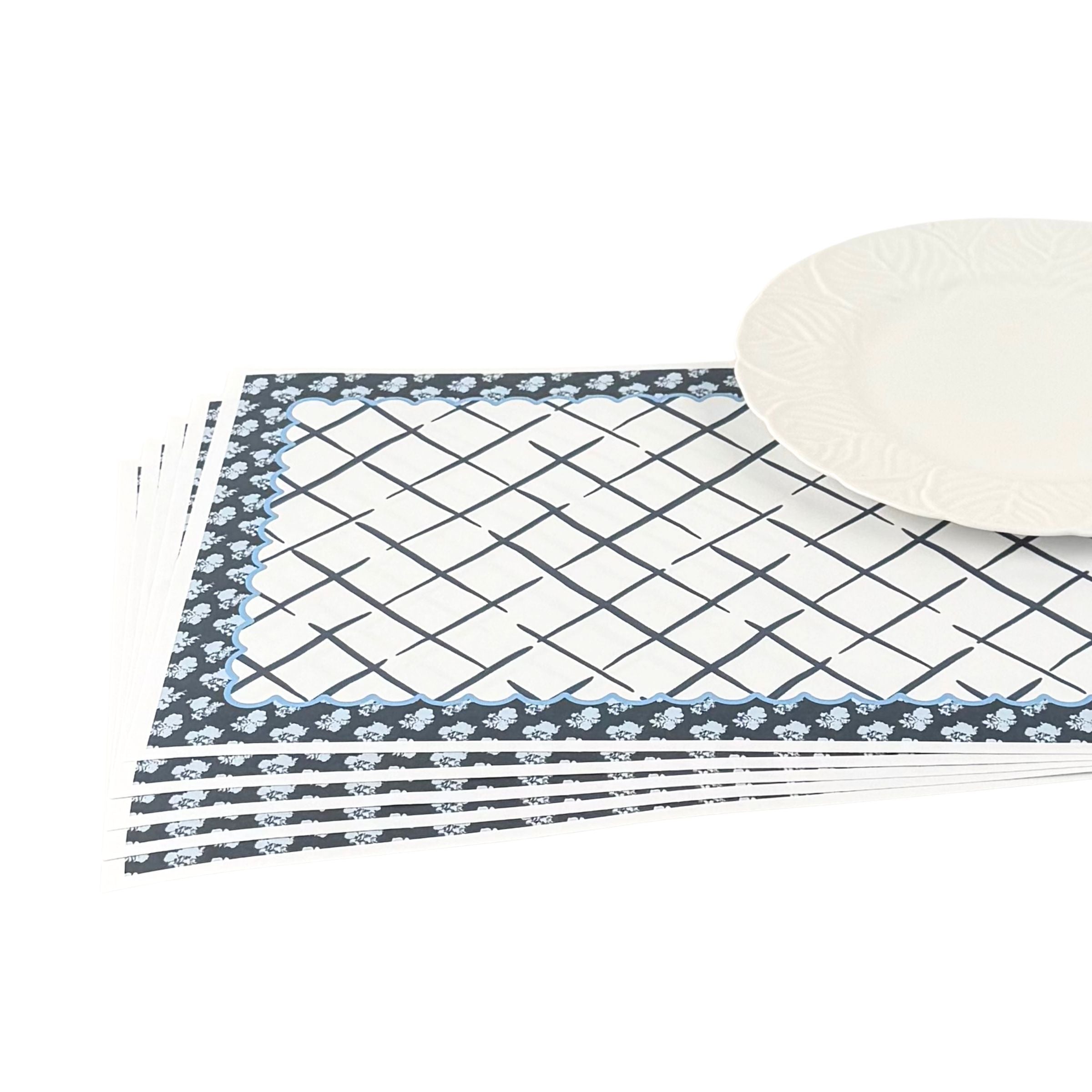 a set of blue and white floral paper placemats lying on a white surface with a white plate on top
