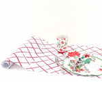 trellis pattern red and white paper table runner for summer bbqs on a white background and red glass and red plate resting on it. 