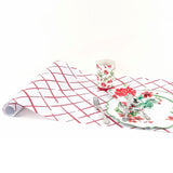 trellis pattern red and white paper table runner for summer bbqs on a white background and red glass and red plate resting on it. 