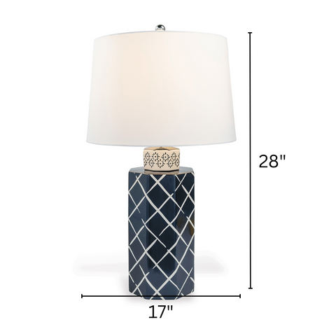 A navy  table lamp with a navy blue porcelain base featuring a white lattice pattern and a plain white lampshade with arrows denoting dimensions 28" high and 17" wide