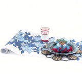 A blue and white floral paper table with blue hydrangea pattern on a white background with a red glass and blue plate resting on it. 