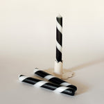 Three black-and-white taper candles on a light background, one standing upright and two lying horizontally.