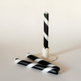 Three black-and-white taper candles on a light background, one standing upright and two lying horizontally.
