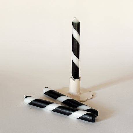 Three black-and-white taper candles on a light background, one standing upright and two lying horizontally.