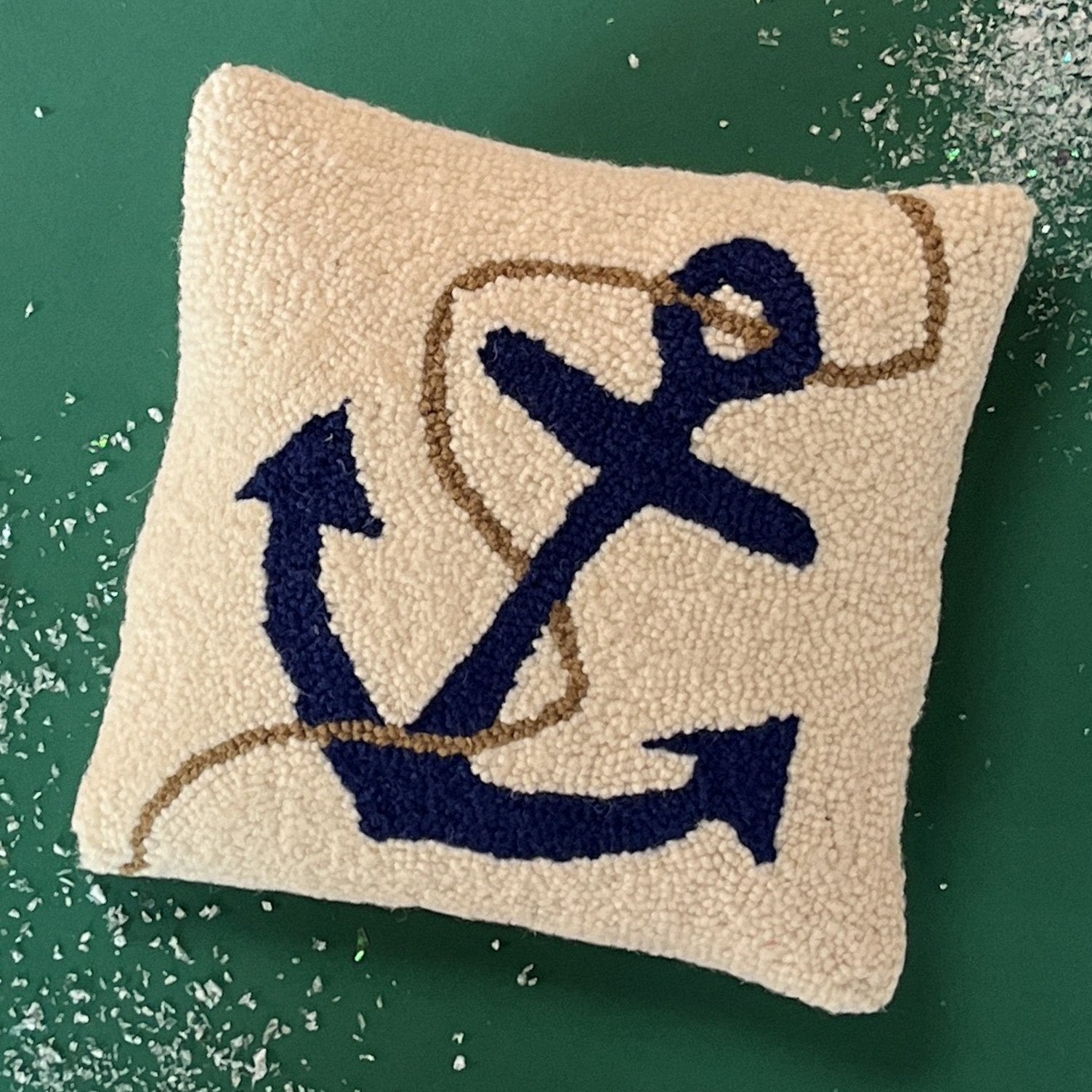 A white pillow featuring a dark blue anchor design with a tan rope wrapped around it.