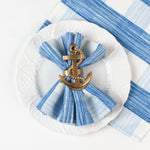 Blue and white striped cloth napkin styled on a white plate with a gold anchor napkin ring.