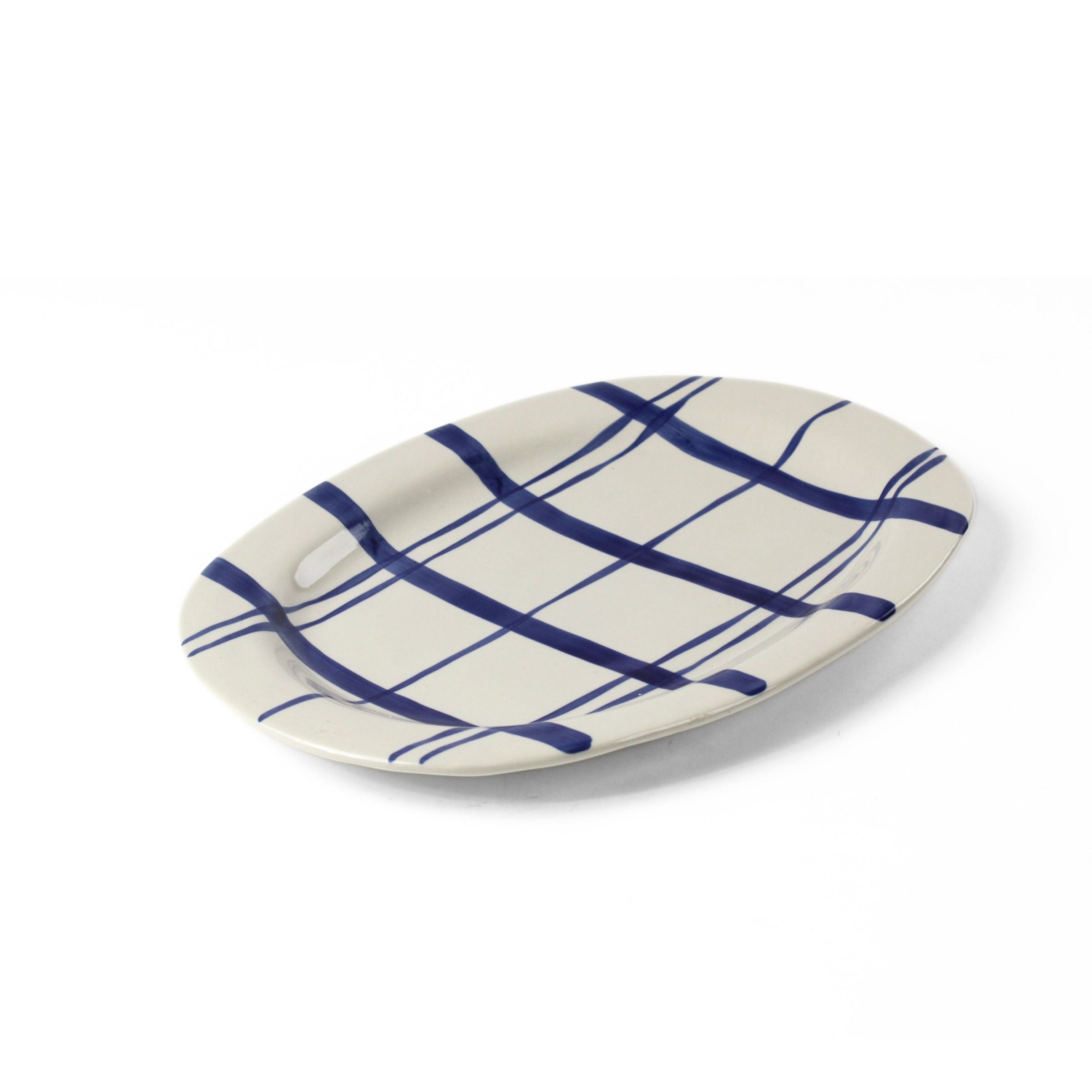 Oval ceramic serving platter with hand-painted blue plaid pattern on a white background viewed at an angled side perspective.
