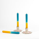 a pair of yellow and blue taper candles in white ceramic candle holders and 1 candle lying down
