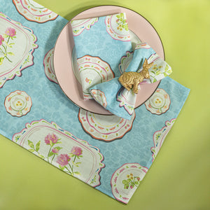 blue vintage plates fabric table runner and napkins with a pink plate and bunny napkin rings on a green background. 
