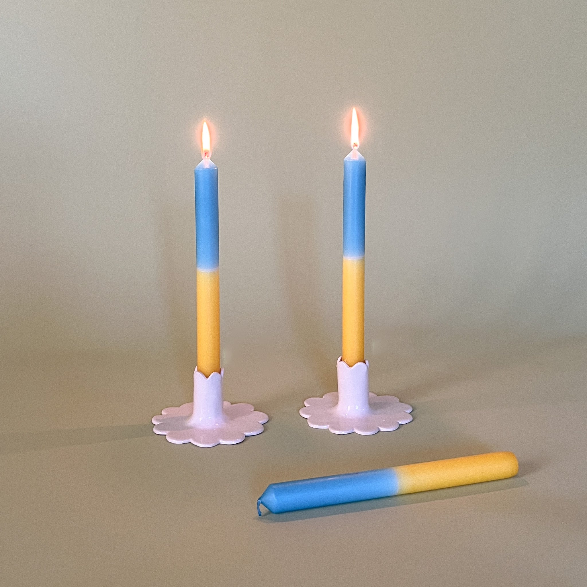 a pair of yellow and blue taper candles in white ceramic candle holders