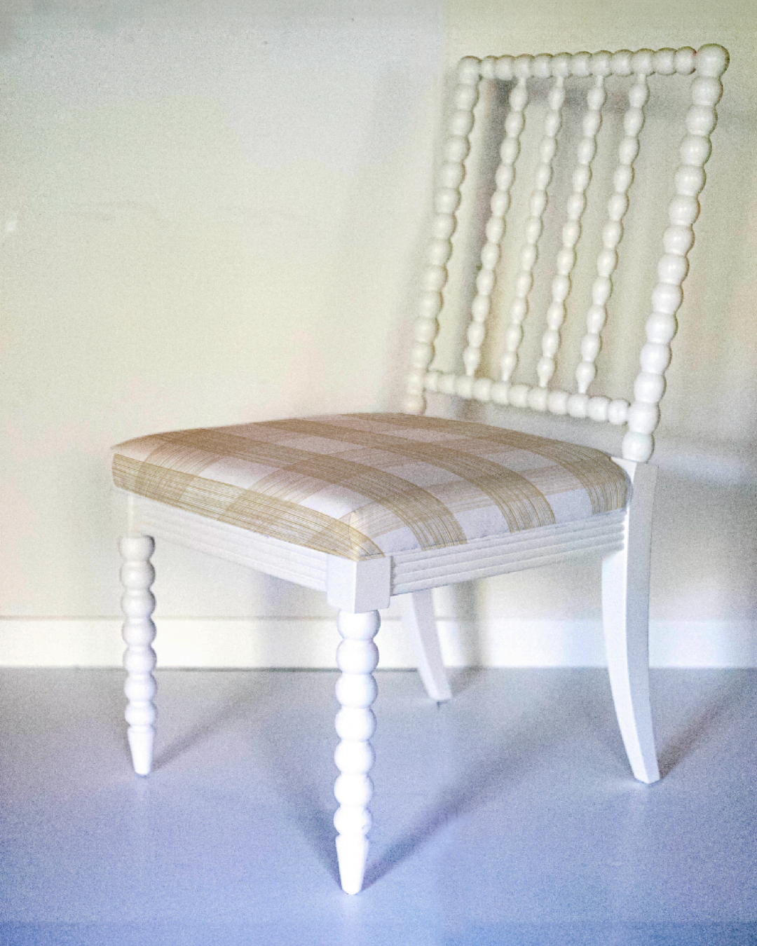 a white bobbin chair with a beige plaid seat.