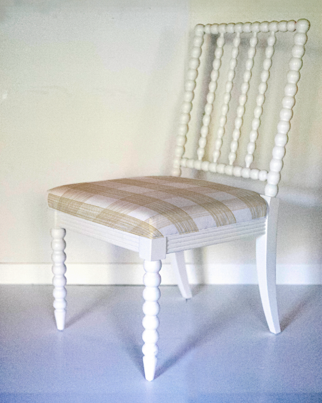 a white bobbin chair with a beige plaid seat. 