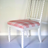 A white bobbin chair with a red plaid seat.