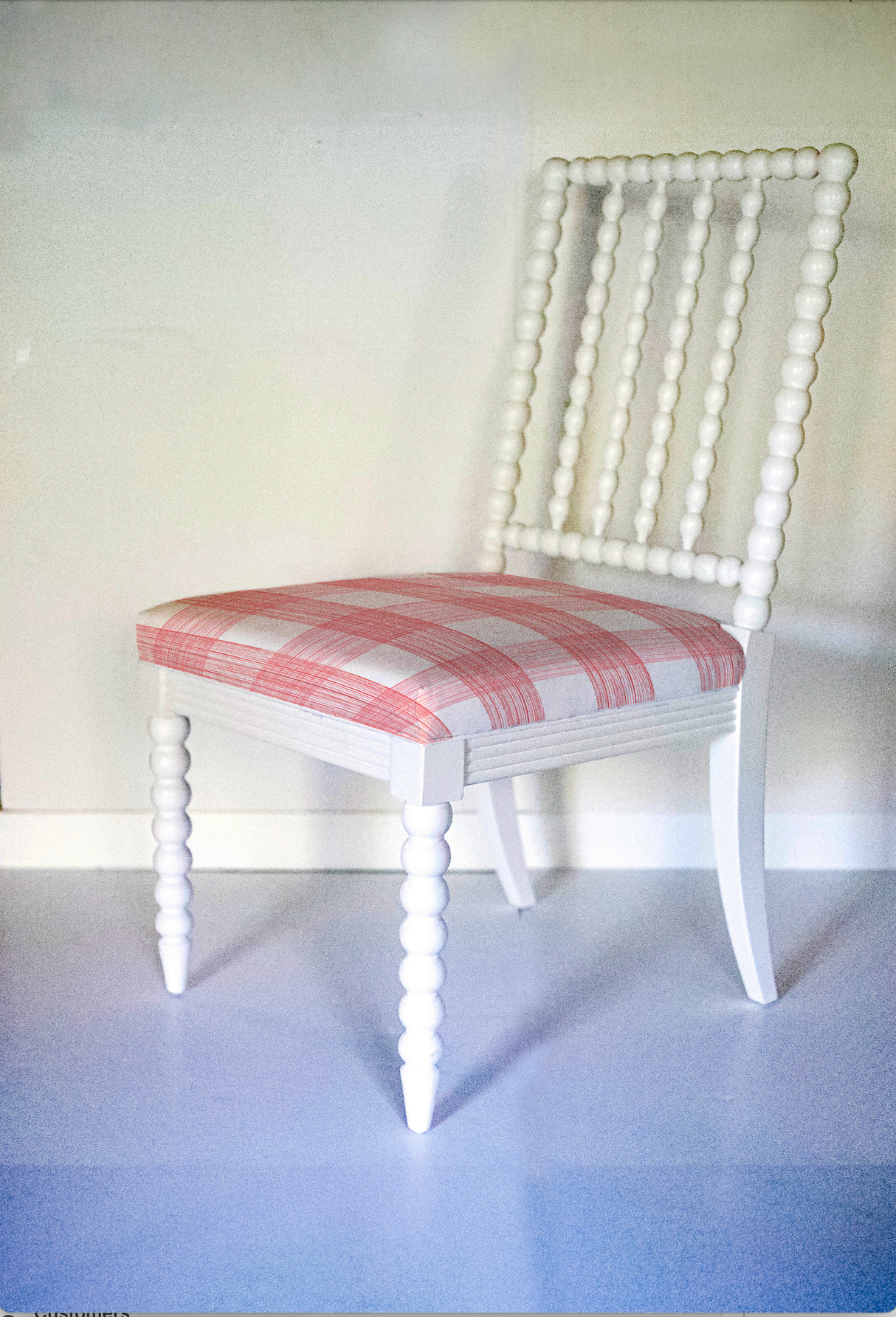 A white bobbin chair with a red plaid seat.