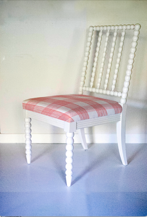 A white bobbin chair with a red plaid seat.