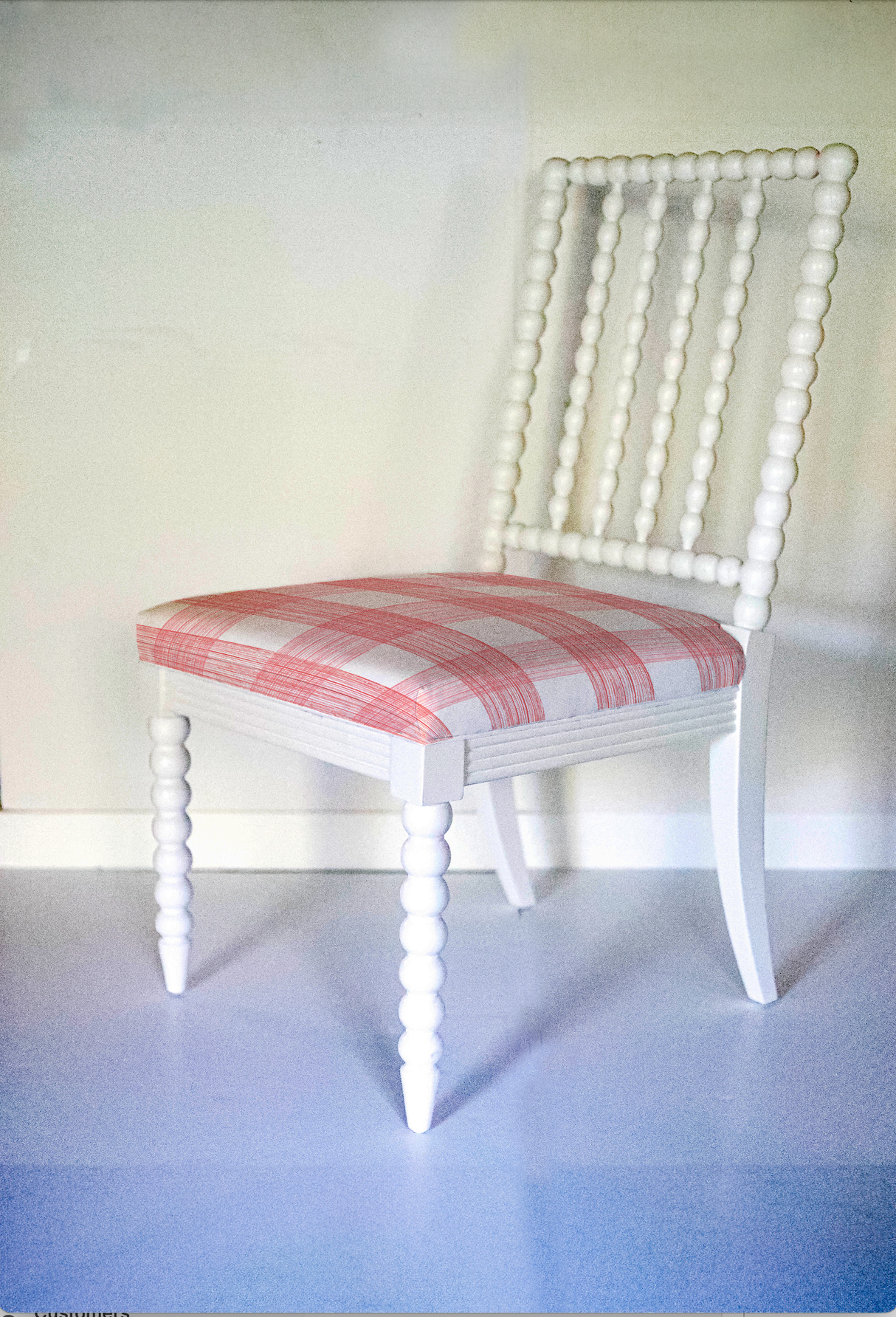 A white bobbin chair with a red plaid seat. 