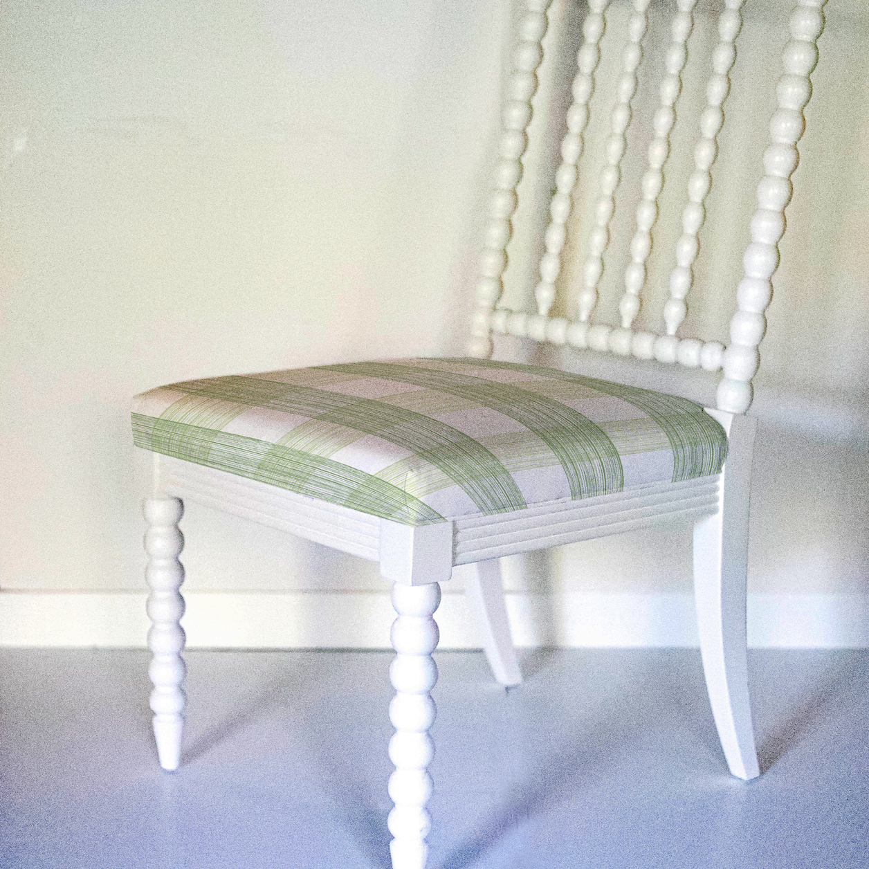 A white bobbin chair with a green plaid seat.